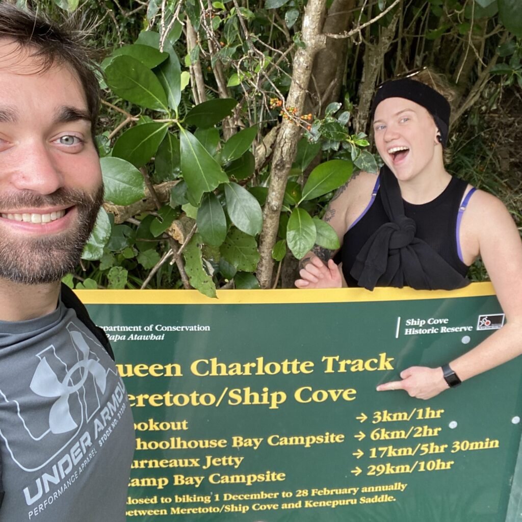 Jess and Ben at the Ship Cove sign at the start/end of the Queen Charlotte Track in the Marlborough Sounds, New Zealand.