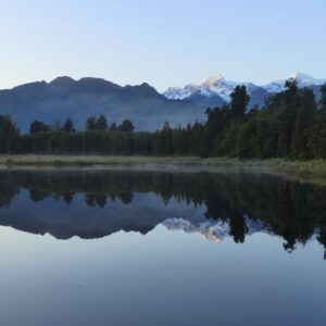 A lake reflecting the surrounding trees and snow capped mountains perfectly upon its surface.