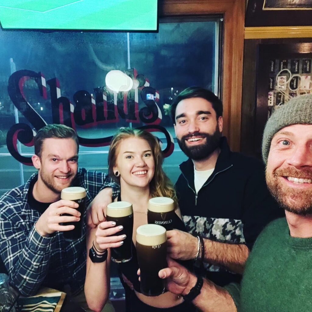 The image is a selfie inside an Irish bar called Paddy McNaughton's in Christchurch (New Zealand) of four people holding up their Guinness.