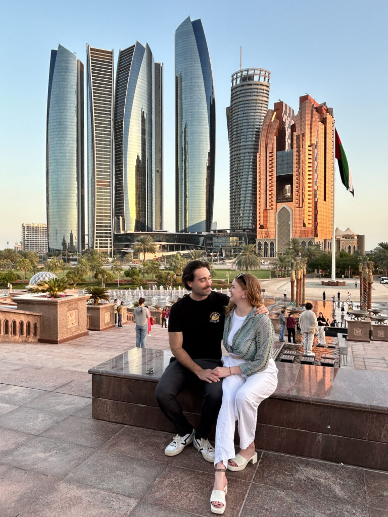 a young couple sat on the edge of a step with large mirrored sky scrapers in the background