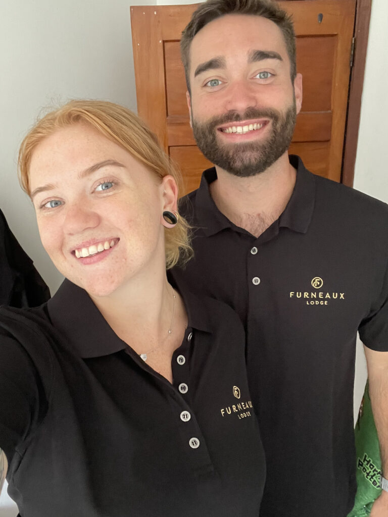 A selfie of two people in the 2023 Furneaux Lodge staff uniform on. Both people are smiling and look happy.