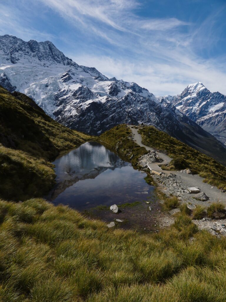 a View of sealy tarn with a glacier and Aoraki mount cook in the background with a winding path leading toward a smalll picnic in the distance with a view of mount cook