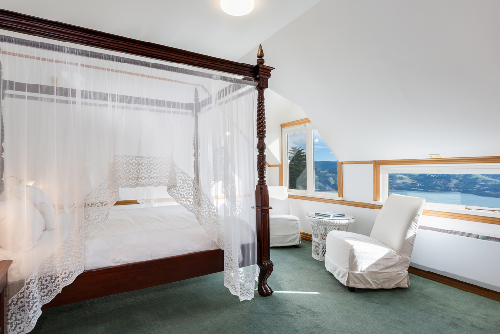 A white room with a ark brown 4 poster bed and incredible views out of the windows