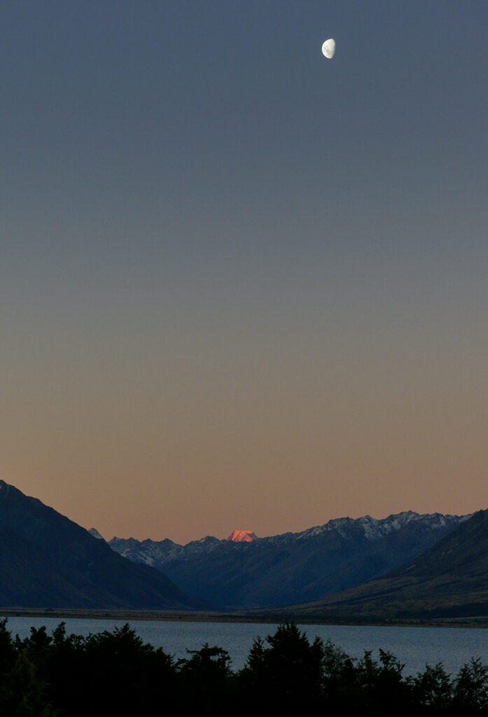 Sunset over Lake Ōhau, with a half moon above the red peak that is Mount Cook.